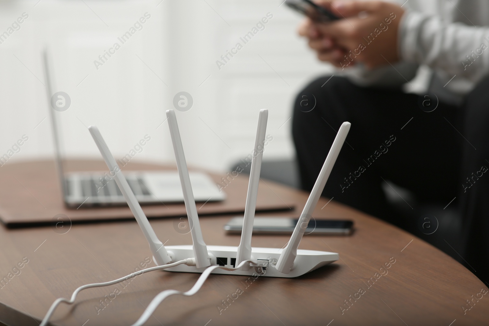 Photo of Man with smartphone and laptop working at wooden table, focus on Wi-Fi router