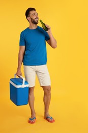 Photo of Happy man with cool box drinking beer on yellow background