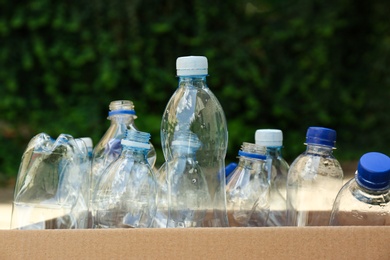 Photo of Cardboard box with used plastic bottles outdoors. Recycle concept