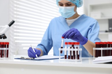 Laboratory testing. Doctor with blood samples in tubes at white table indoors, selective focus