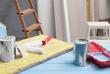 Photo of Cans of paint, roller and tray on blue wooden table indoors