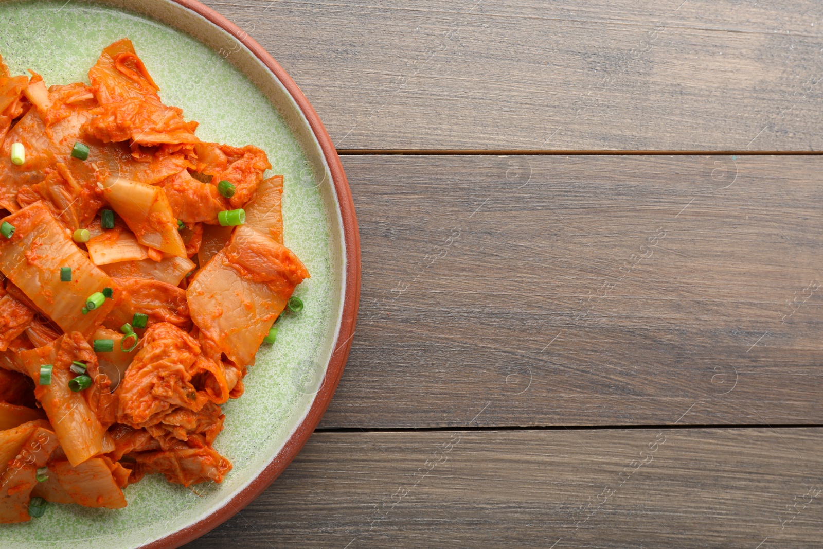 Photo of Plate of delicious kimchi with Chinese cabbage on wooden table, top view. Space for text