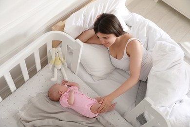 Photo of Young mother resting near crib with sleeping newborn baby at home, above view