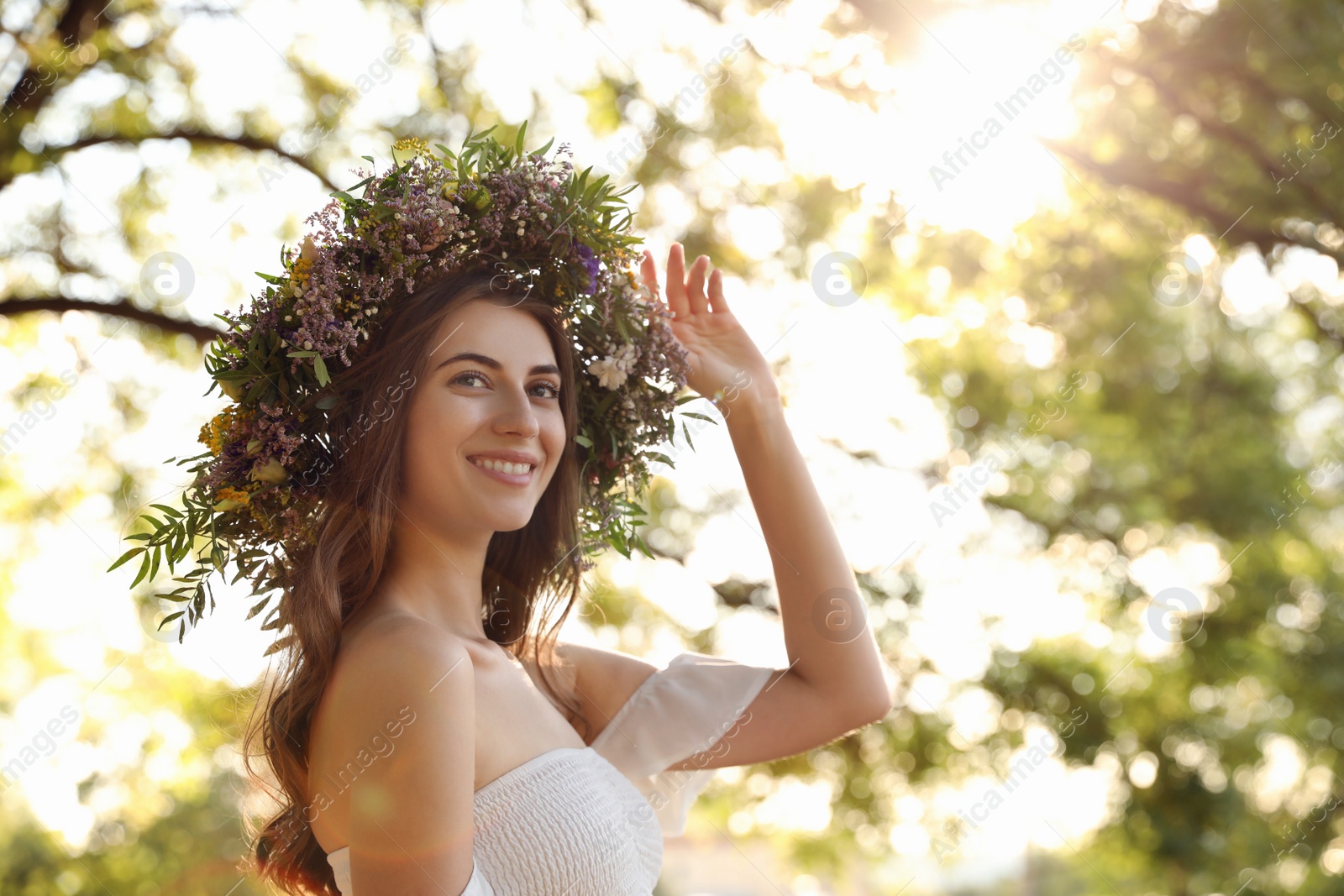 Photo of Young woman wearing wreath made of beautiful flowers outdoors on sunny day