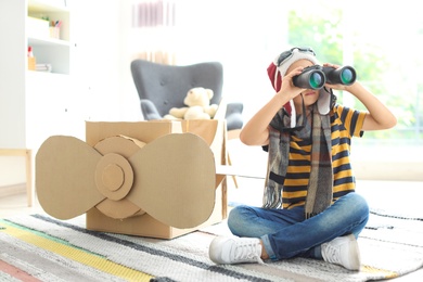Photo of Adorable little child playing with binoculars and cardboard airplane indoors
