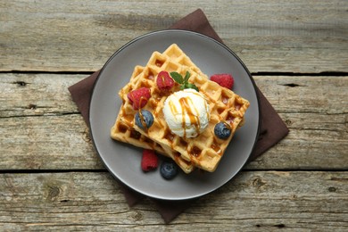 Photo of Delicious Belgian waffles with ice cream, berries and caramel sauce on wooden table, top view