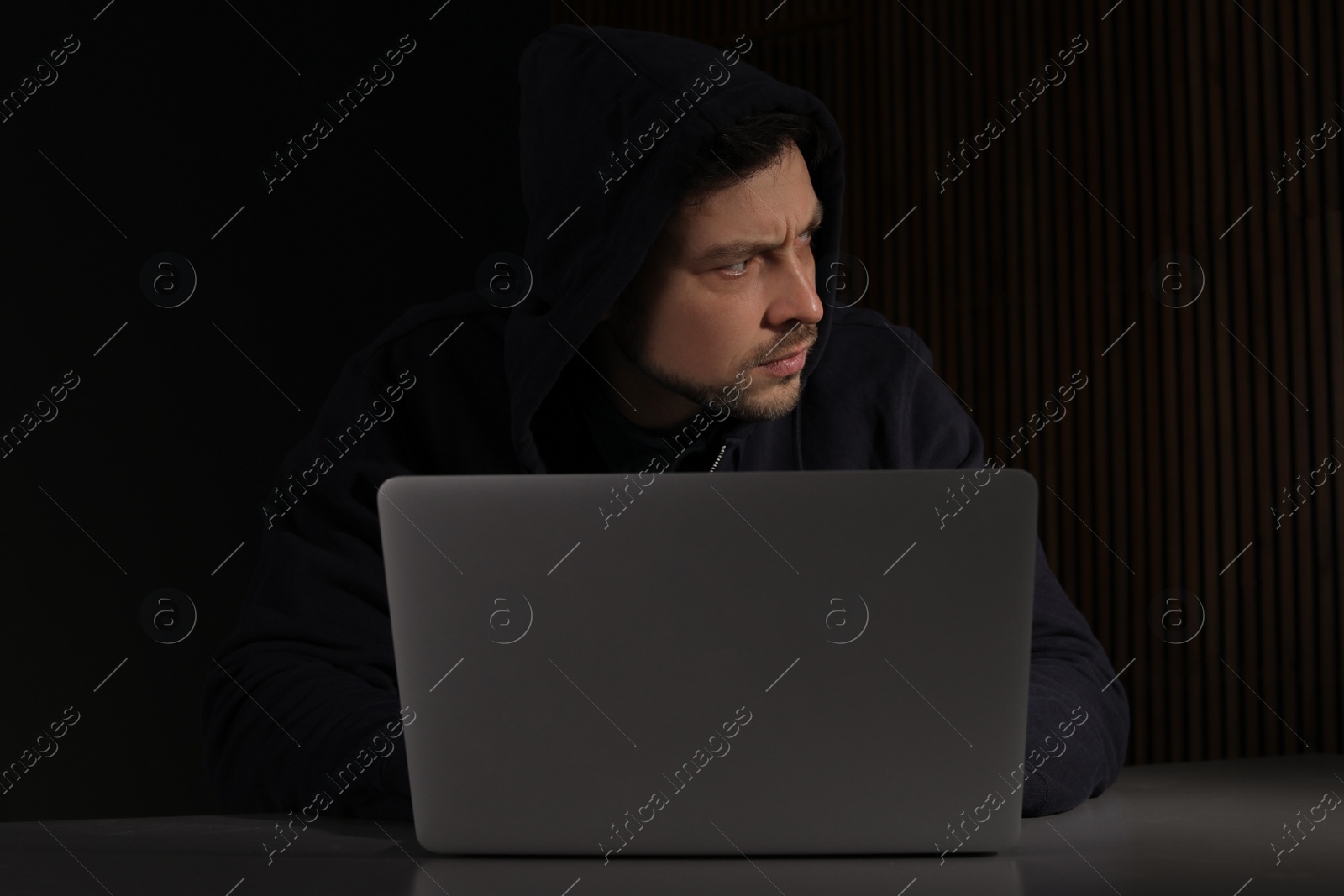 Photo of Man using laptop in dark room. Criminal offence