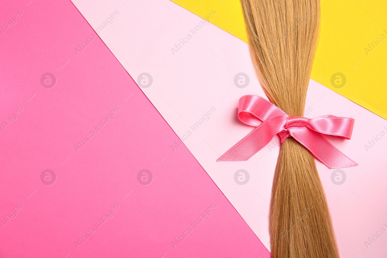 Photo of Blond hair tied with ribbon and space for text on color background, top view