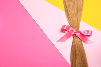 Blond hair tied with ribbon and space for text on color background, top view