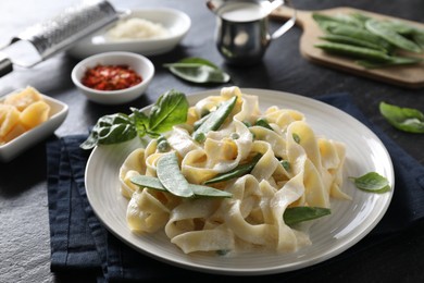 Photo of Delicious pasta with green peas and creamy sauce on black table