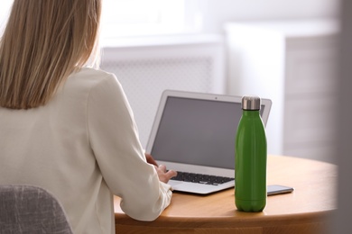 Photo of Woman with thermo bottle working at table in modern office, closeup