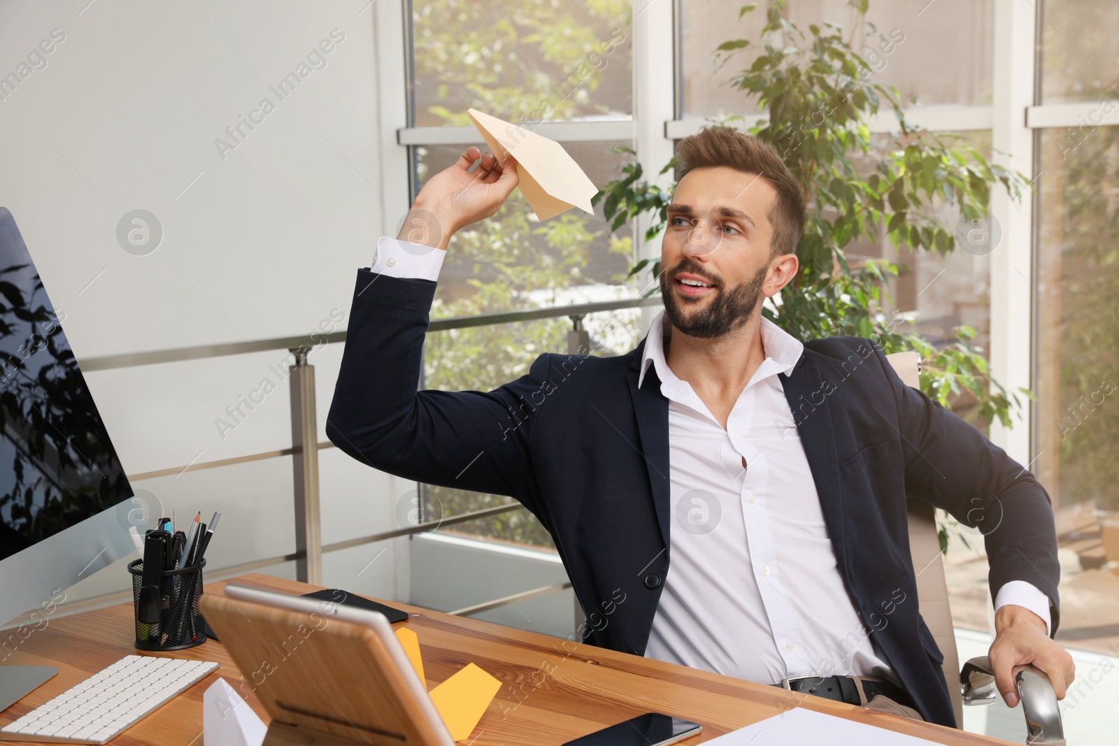 Photo of Handsome businessman playing with paper plane at desk in office