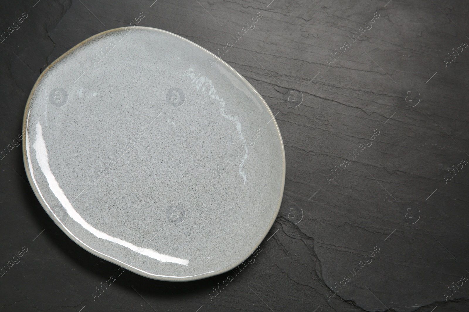 Photo of One ceramic plate on black textured table, top view. Space for text