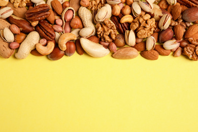 Photo of Different delicious nuts on yellow background, flat lay. Space for text