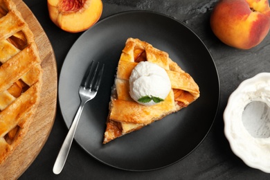 Slice of delicious peach pie with ice cream on black table, flat lay