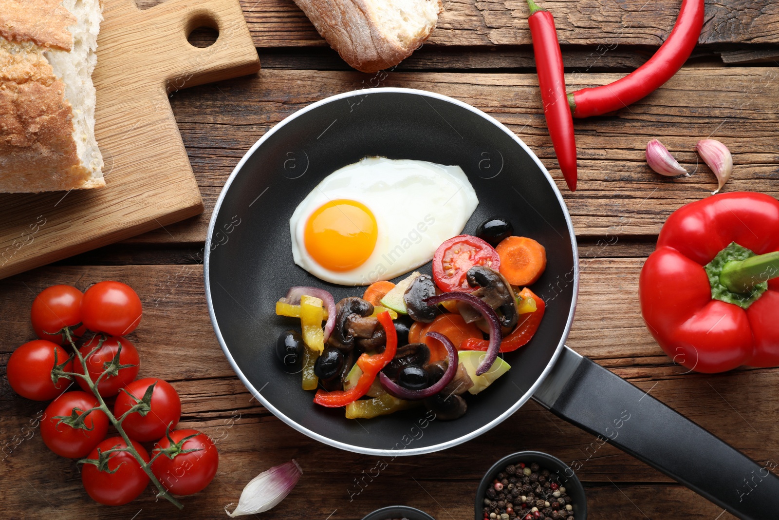 Photo of Tasty fried egg with vegetables in pan and ingredients on wooden table, flat lay