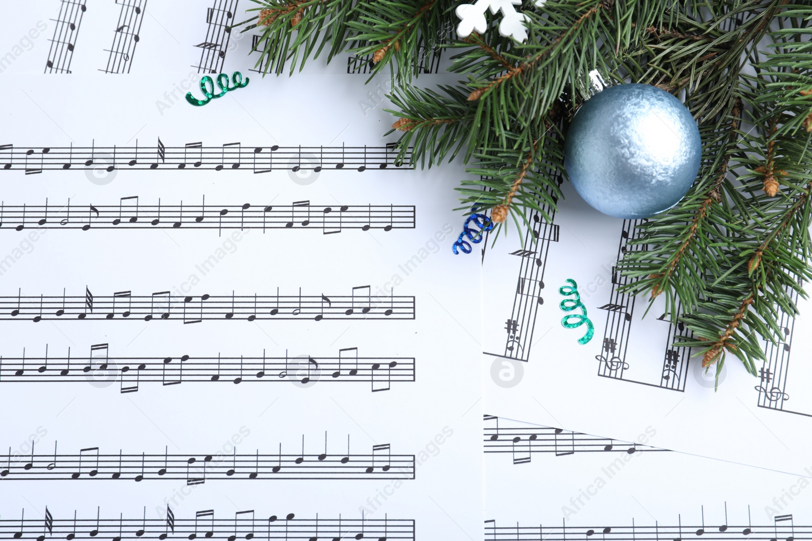 Photo of Fir branches and blue light blue ball on Christmas music sheets, flat lay