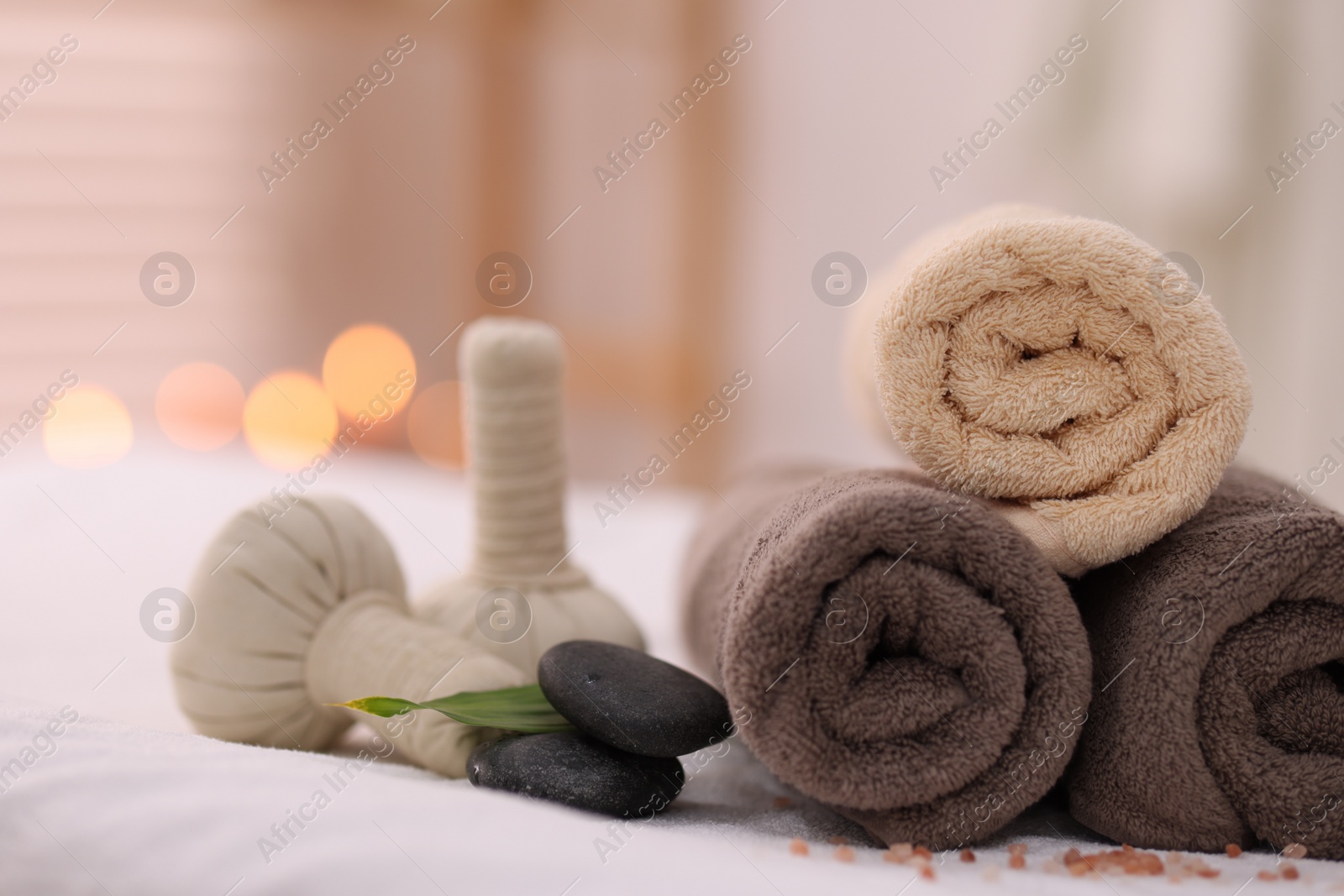 Photo of Spa stones, rolled towels and herbal bags on massage table indoors, closeup