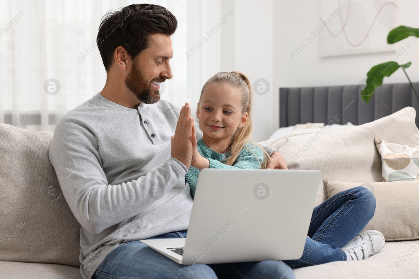 Photo of Happy man and his daughter with laptop on sofa at home