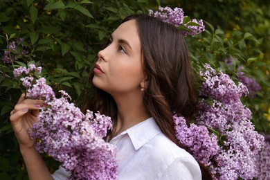 Attractive young woman near blooming lilac bush outdoors