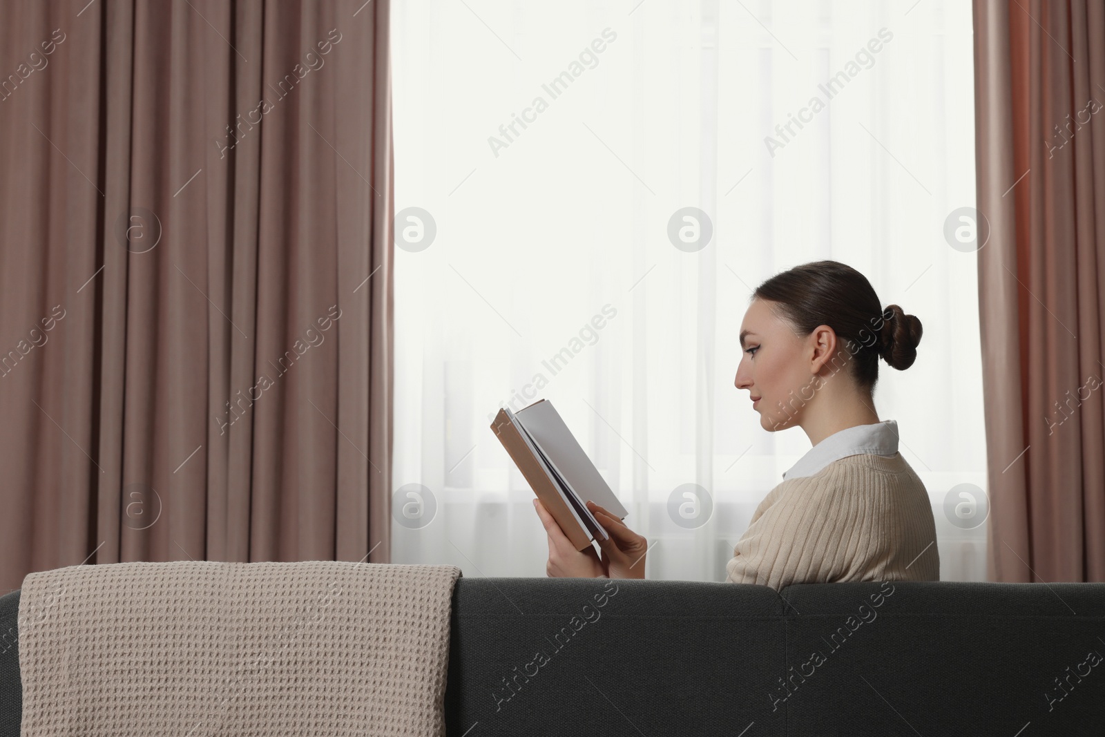 Photo of Woman reading book on sofa near window with stylish curtains at home. Space for text