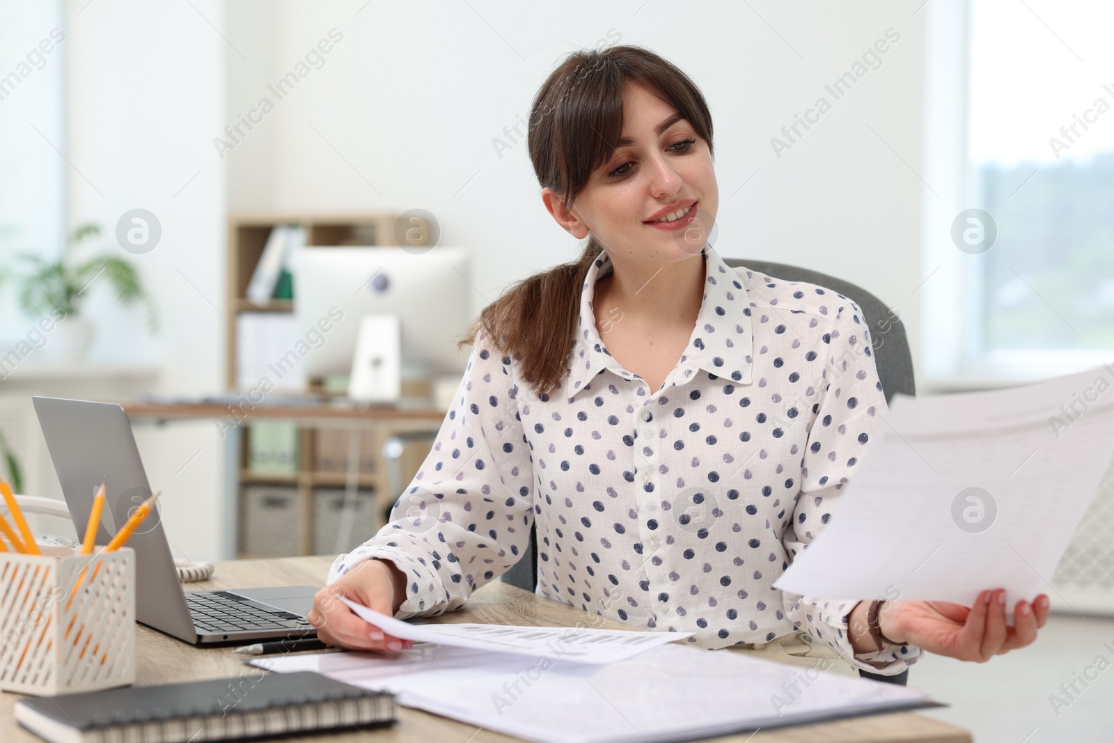 Photo of Smiling secretary doing paperwork at table in office