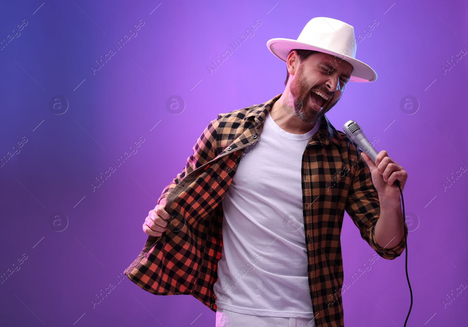 Photo of Emotional man with microphone singing in neon lights. Space for text