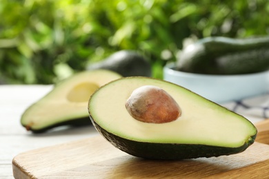 Photo of Half of delicious ripe avocado on wooden board against blurred background