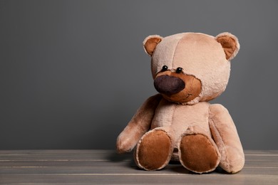 Photo of Cute teddy bear on wooden table near black wall, space for text