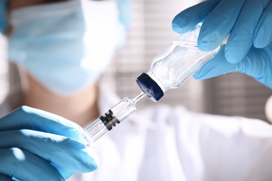 Woman filling syringe with vaccine from vial on blurred background, closeup