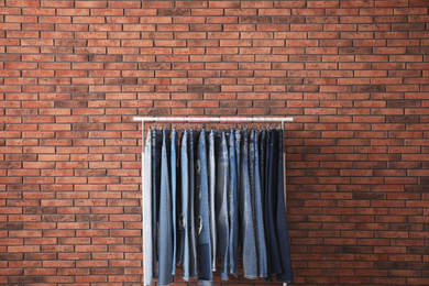 Rack with stylish jeans near brick wall