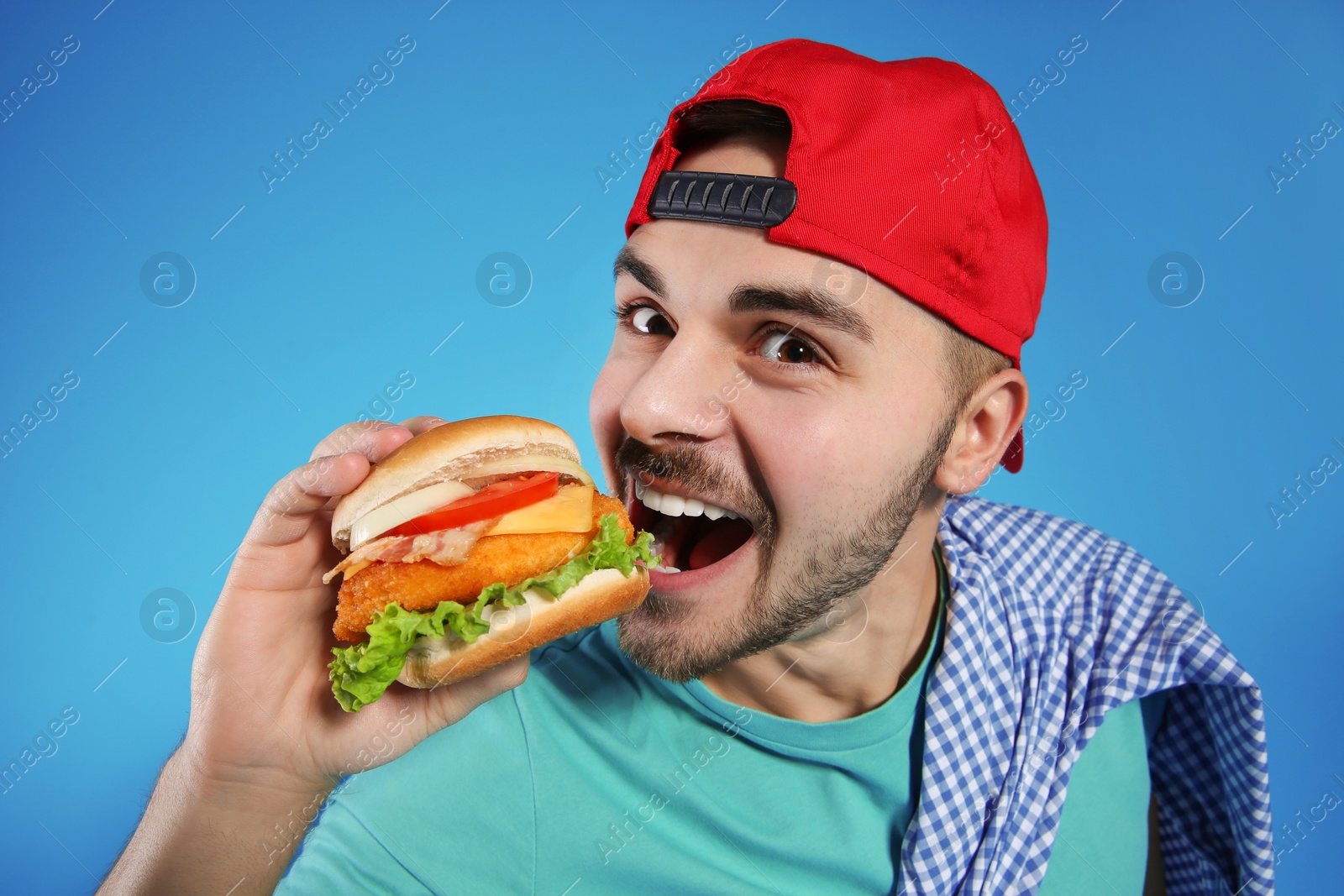 Photo of Handsome man eating tasty burger on color background