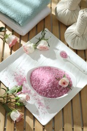 Photo of Bowl of pink sea salt and beautiful roses on wooden table, above view