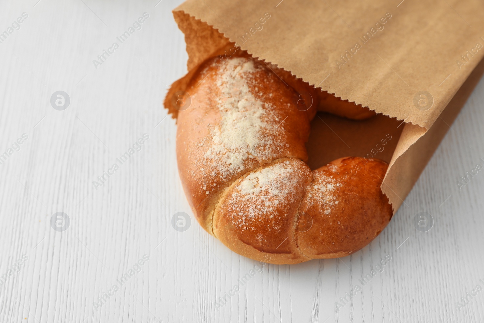 Photo of Paper bag with pastry on light wooden background. Space for text