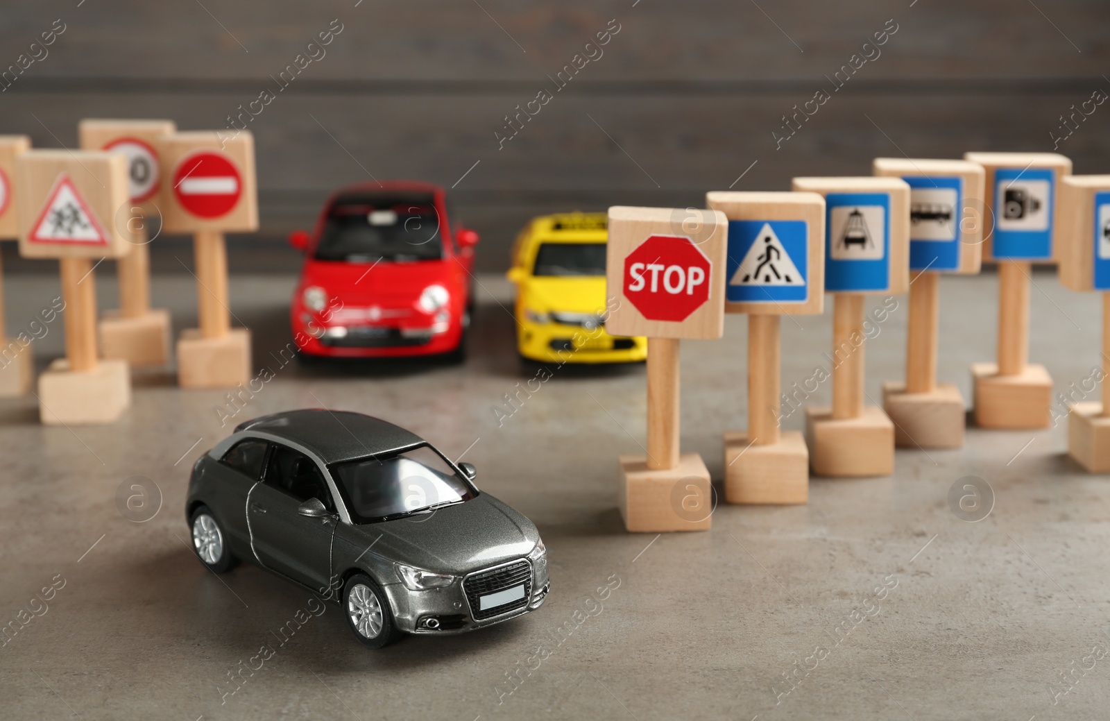 Photo of Many different miniature road signs and cars on grey table. Driving school