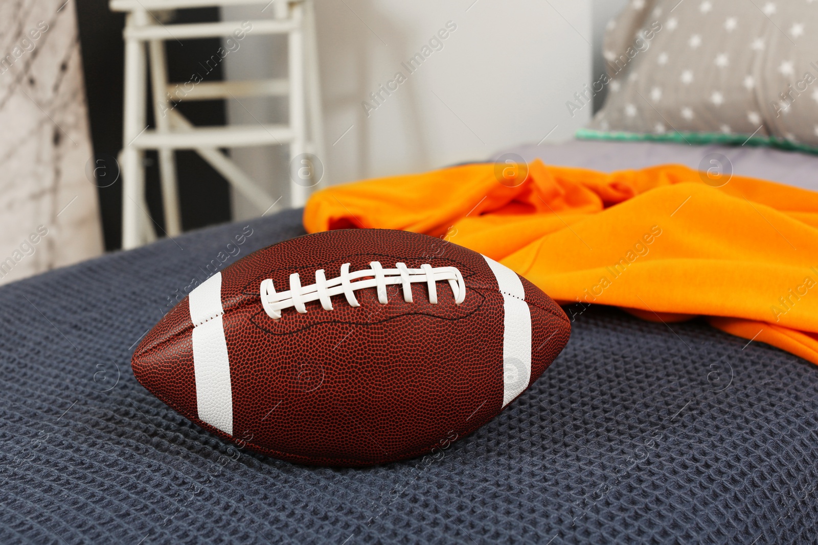 Photo of Comfortable bed with American football ball in room. Interior design