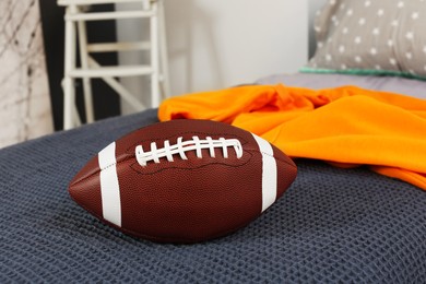 Comfortable bed with American football ball in room. Interior design