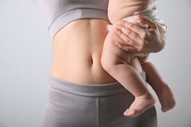 Mother with bare belly holding her baby on light grey background, closeup