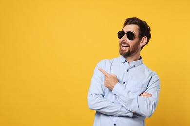 Photo of Portrait of excited bearded man with stylish sunglasses on orange background. Space for text