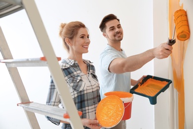 Photo of Happy couple painting wall indoors. Home repair