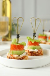 Tasty canapes with salmon, cucumber, bread and cream cheese on white table, closeup