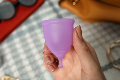 Woman holding violet menstrual cup on blurred background, closeup