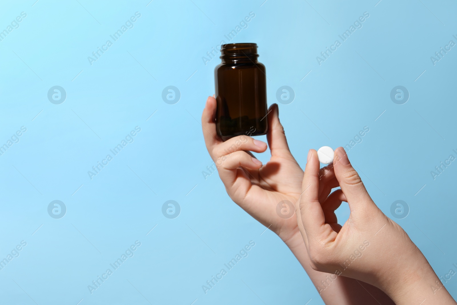 Photo of Woman holding pill and bottle on light blue background, closeup