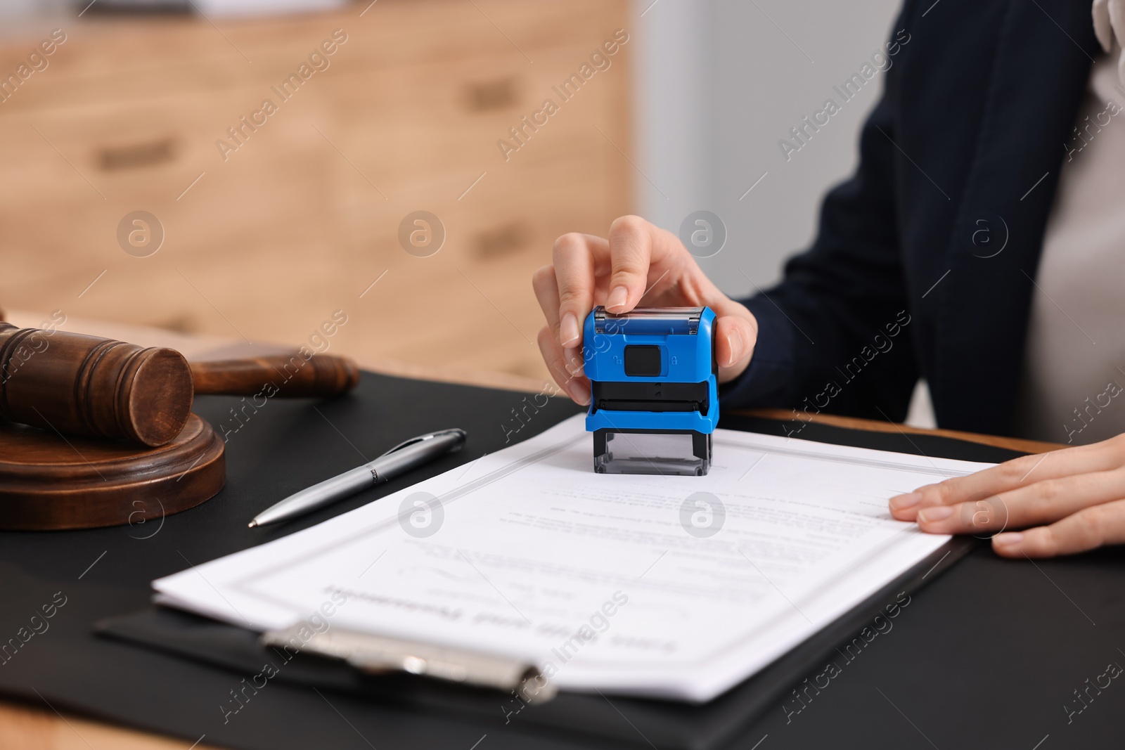 Photo of Notary stamping document at table in office, closeup