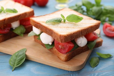 Photo of Delicious Caprese sandwiches with mozzarella, tomatoes, basil and pesto sauce on light blue wooden table, closeup