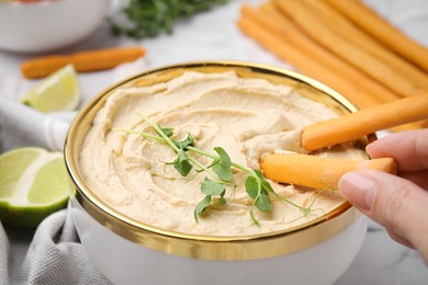 Woman dipping grissini stick into hummus at table, closeup