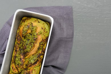 Photo of Freshly baked pesto bread in loaf pan on grey wooden table, top view. Space for text