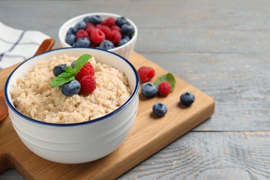 Photo of Tasty oatmeal porridge with berries on grey wooden table. Space for text