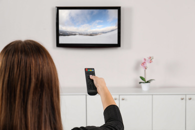 Image of Woman switching channels on TV set with remote control at home