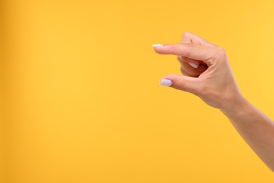 Woman holding something in fingers on yellow background, closeup. Space for text